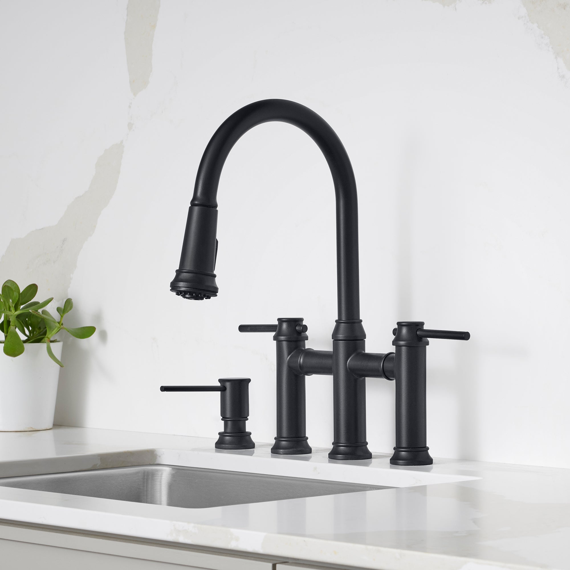 Matte black bridge faucet with pull-down sprayer, two lever handles, and soap dispenser on white countertop.