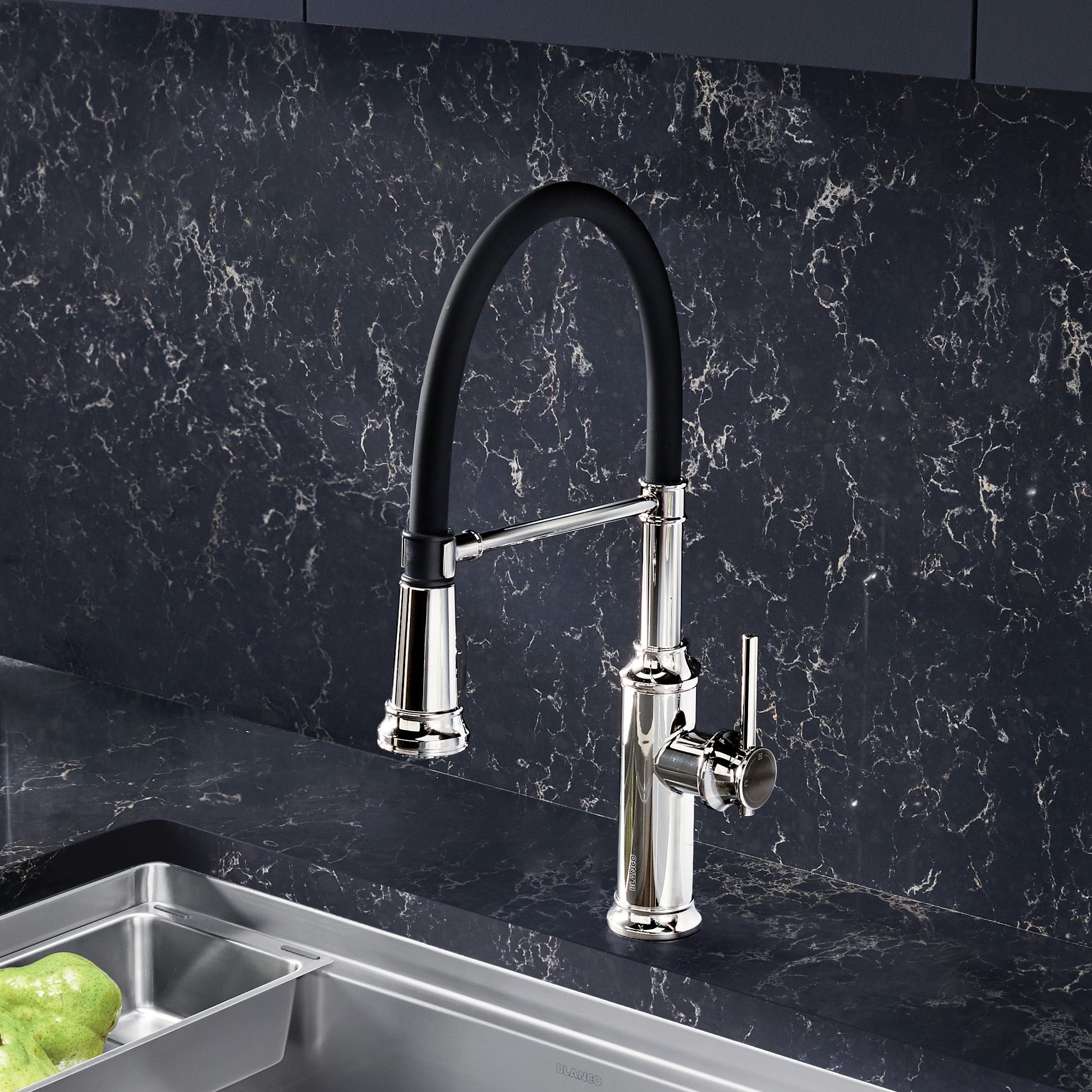 Chrome semi-pro kitchen faucet with black pull-down spray arm over stainless steel sink and dark marble backsplash.