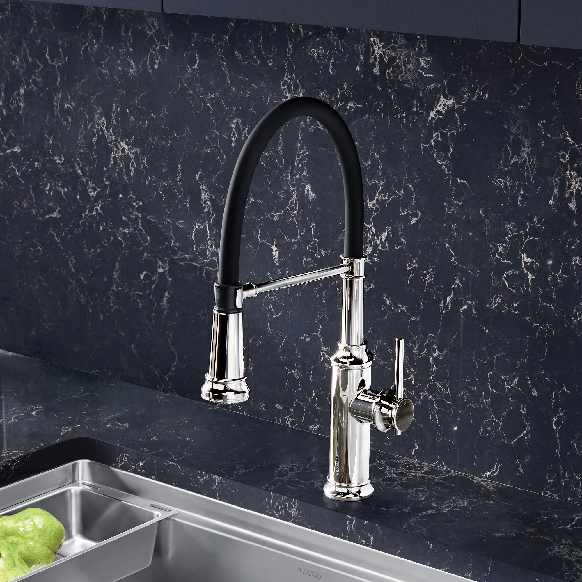 Chrome semi-pro kitchen faucet with black pull-down spray arm over stainless steel sink and dark marble backsplash.