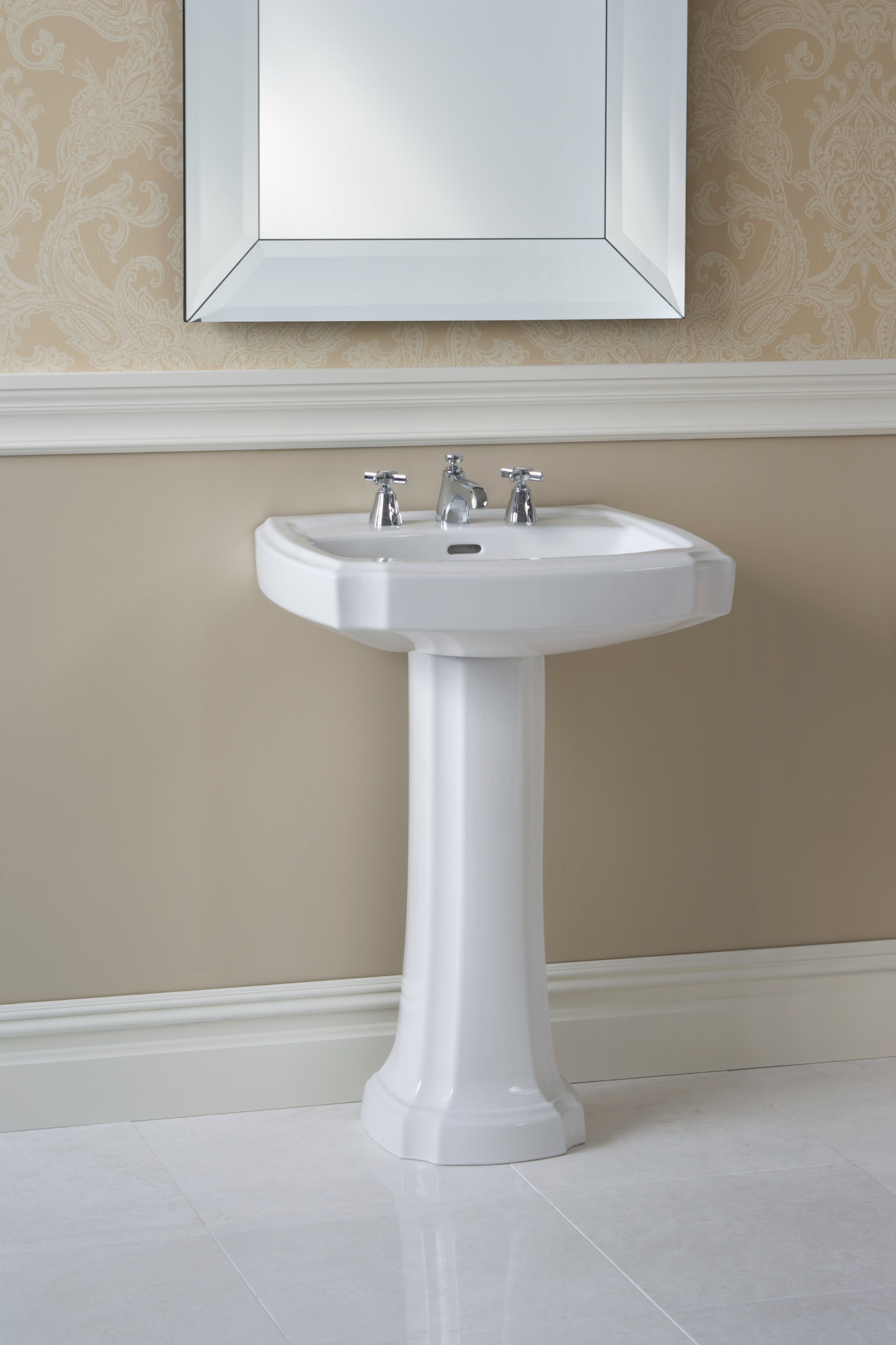 White pedestal bathroom sink with rectangular basin and three-hole faucet mounting, displayed with mirror above.
