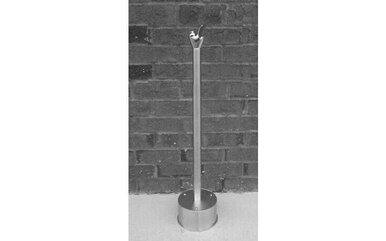 Stainless steel freestanding drinking fountain with tall cylindrical post and round base against brick wall background.
