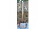 Stainless steel freestanding outdoor shower with curved hose and circular base mounted against stone wall.