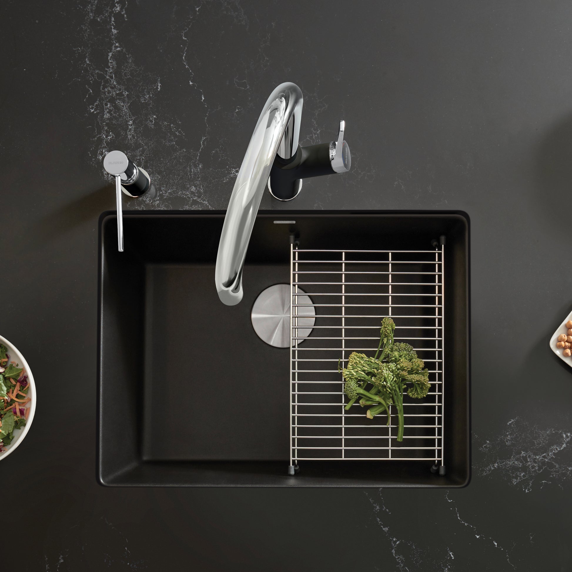 Coal black single bowl kitchen sink with stainless steel faucet, drain, and wire grid strainer insert, shown from above.