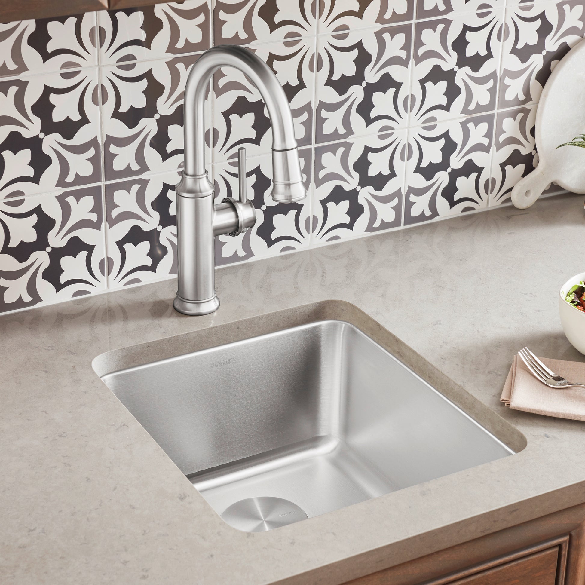 Stainless steel undermount bar sink with single basin installed beneath countertop, paired with chrome faucet.