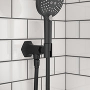 Matte black handshower holder with outlet mounted on white subway tile wall, featuring round perforated showerhead above.