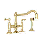 Polished brass bridge kitchen faucet with dual handles, curved spout, and separate side spray attachment.