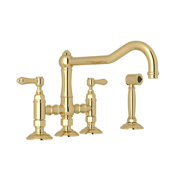 Polished brass bridge kitchen faucet with dual handles, curved spout, and separate side spray attachment.