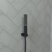 Matte black rectangular handheld showerhead with perforated nozzle mounted on wall tile with attached hose.