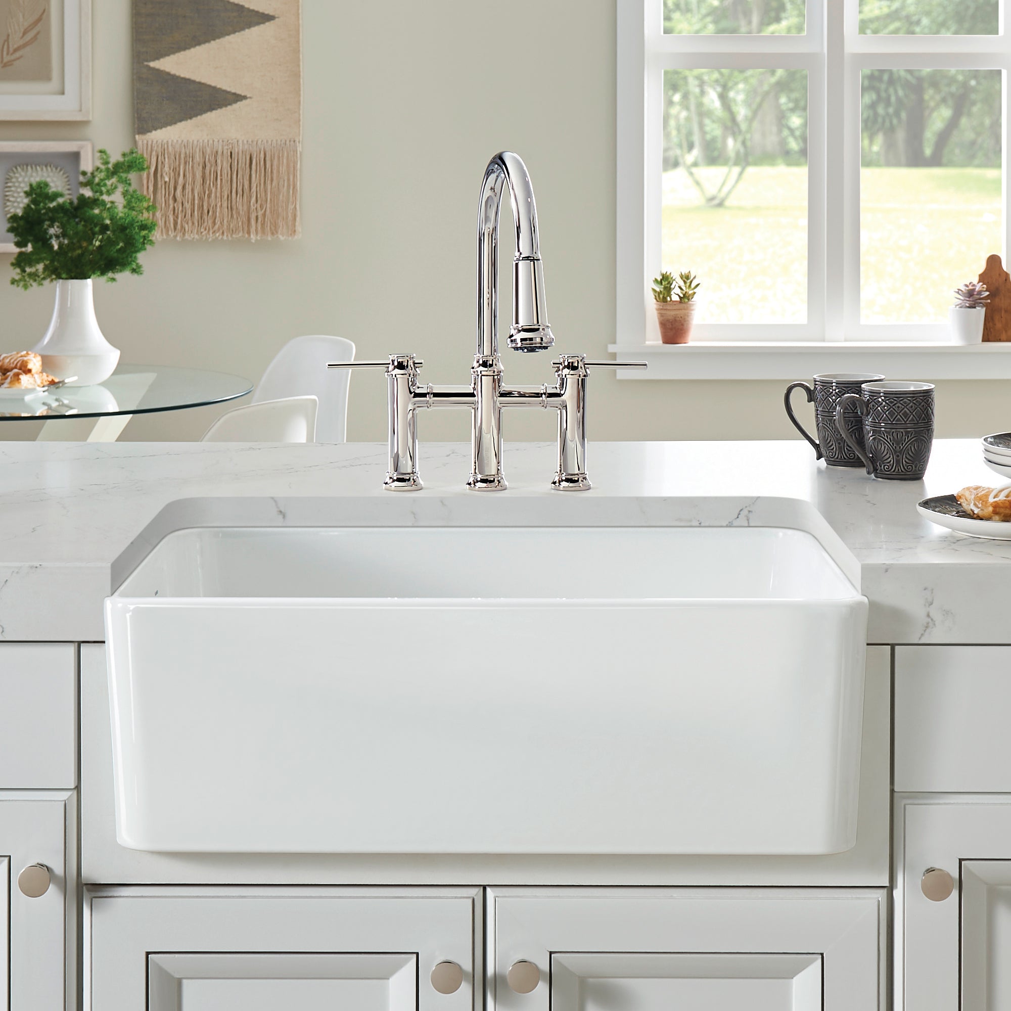 White ceramic farmhouse sink with single bowl and chrome bridge faucet installed in marble countertop.
