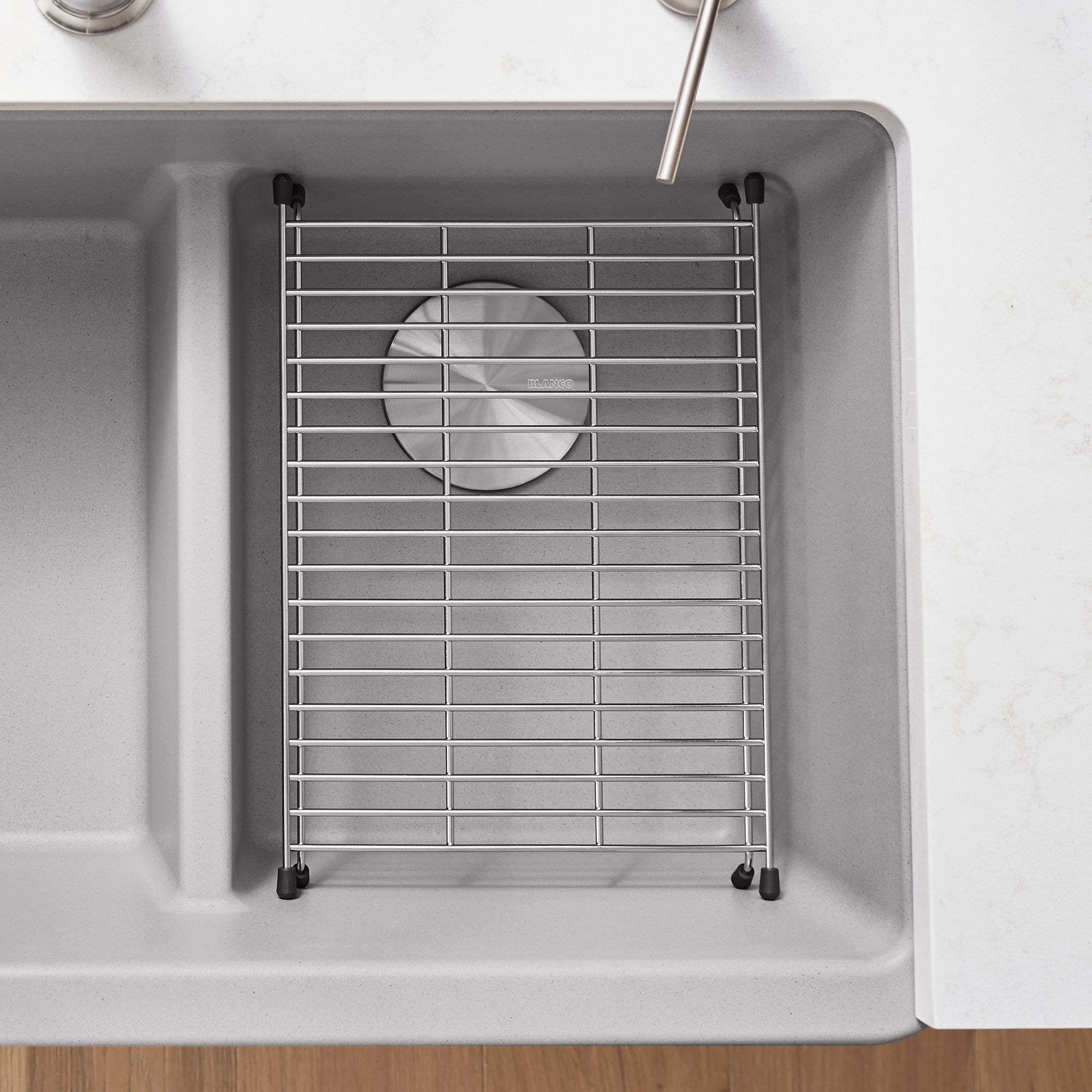 Stainless steel grid with horizontal bars and circular center opening, positioned in gray kitchen sink with black mounting cl