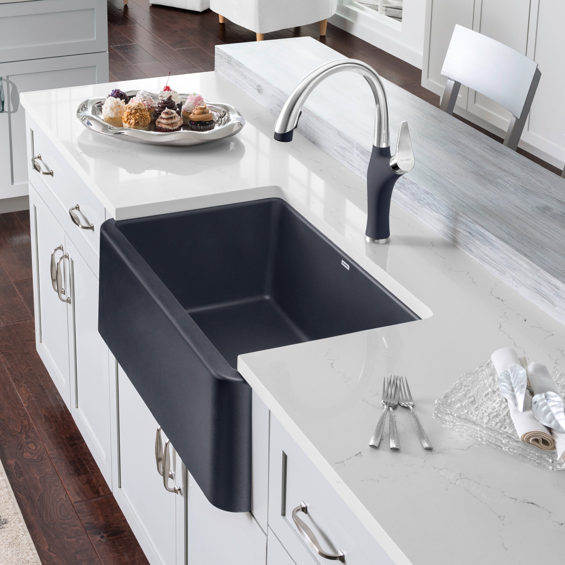 Anthracite apron front kitchen sink with curved chrome faucet installed in white countertop.