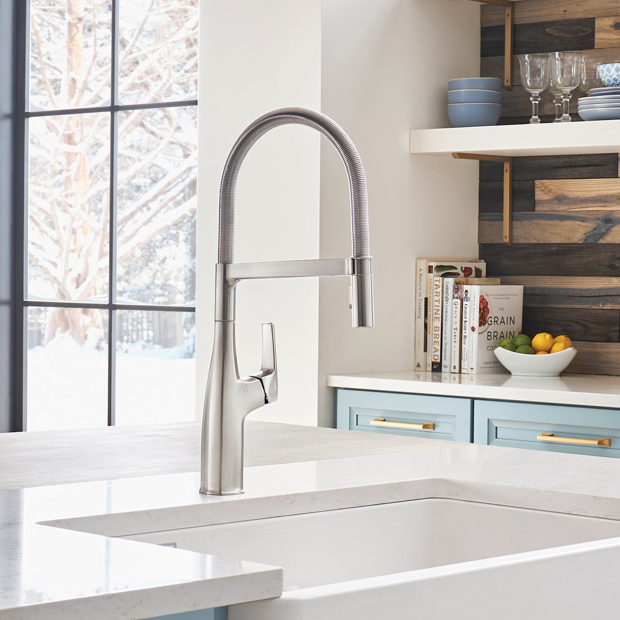 Stainless steel semi-pro kitchen faucet with high arched spout and pull-down spray head mounted above white sink.