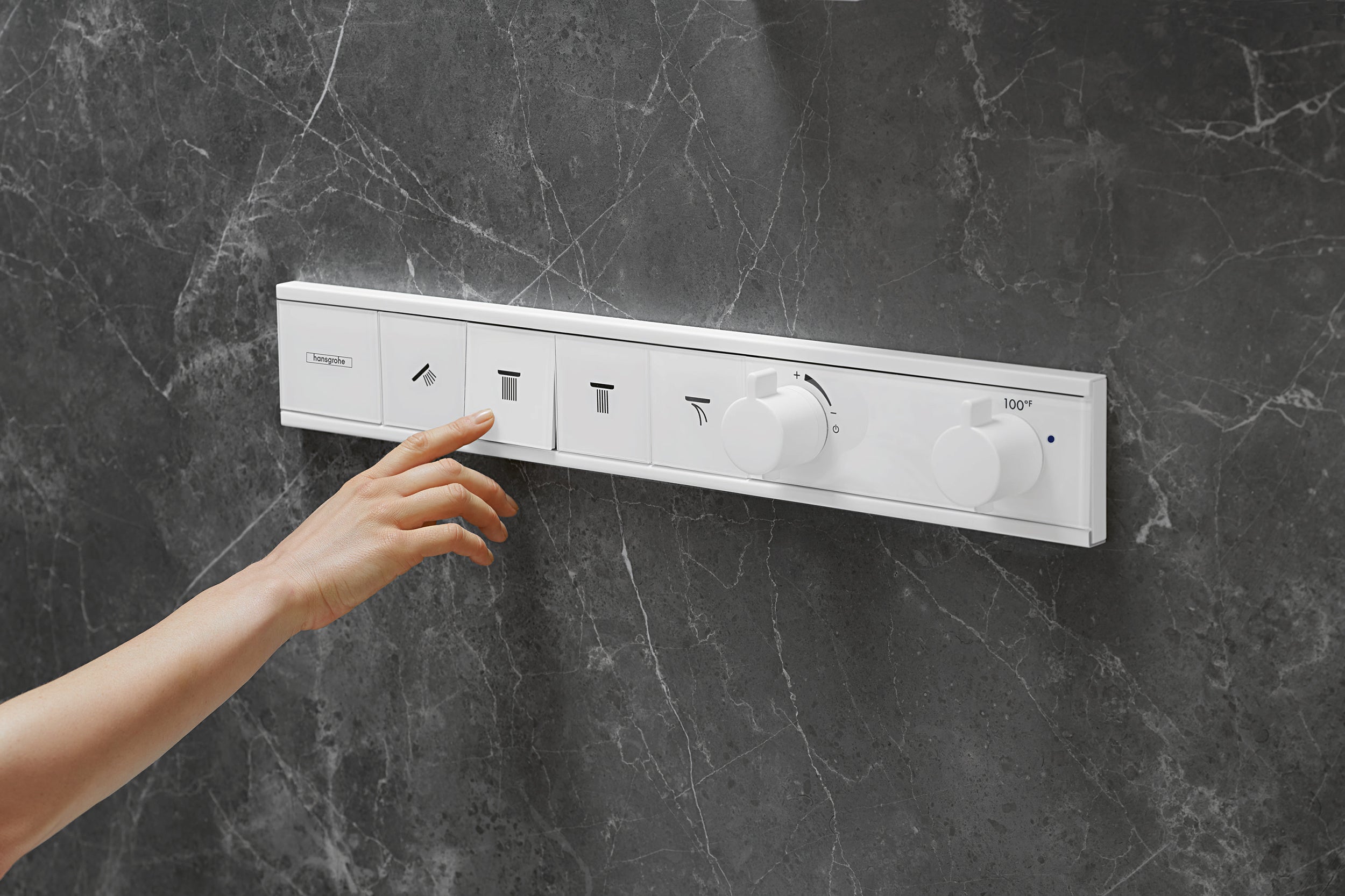 Matte white Hansgrohe thermostatic shower trim with multiple function buttons and rotary controls mounted on dark marble wall