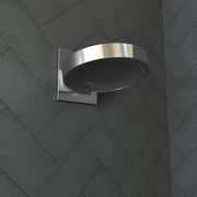 Chrome wall-mounted shower head with round black perforated face and rectangular trim plate on herringbone tile wall.