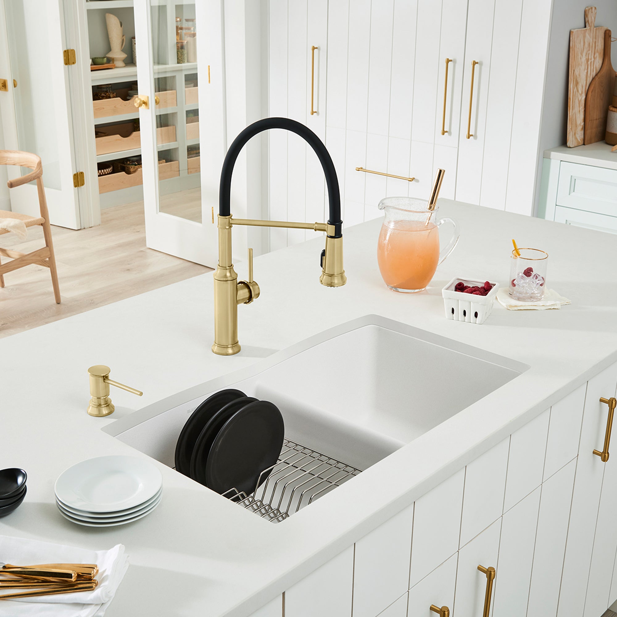 White undermount double bowl kitchen sink with dish rack insert and brass faucet with black handle in modern kitchen.