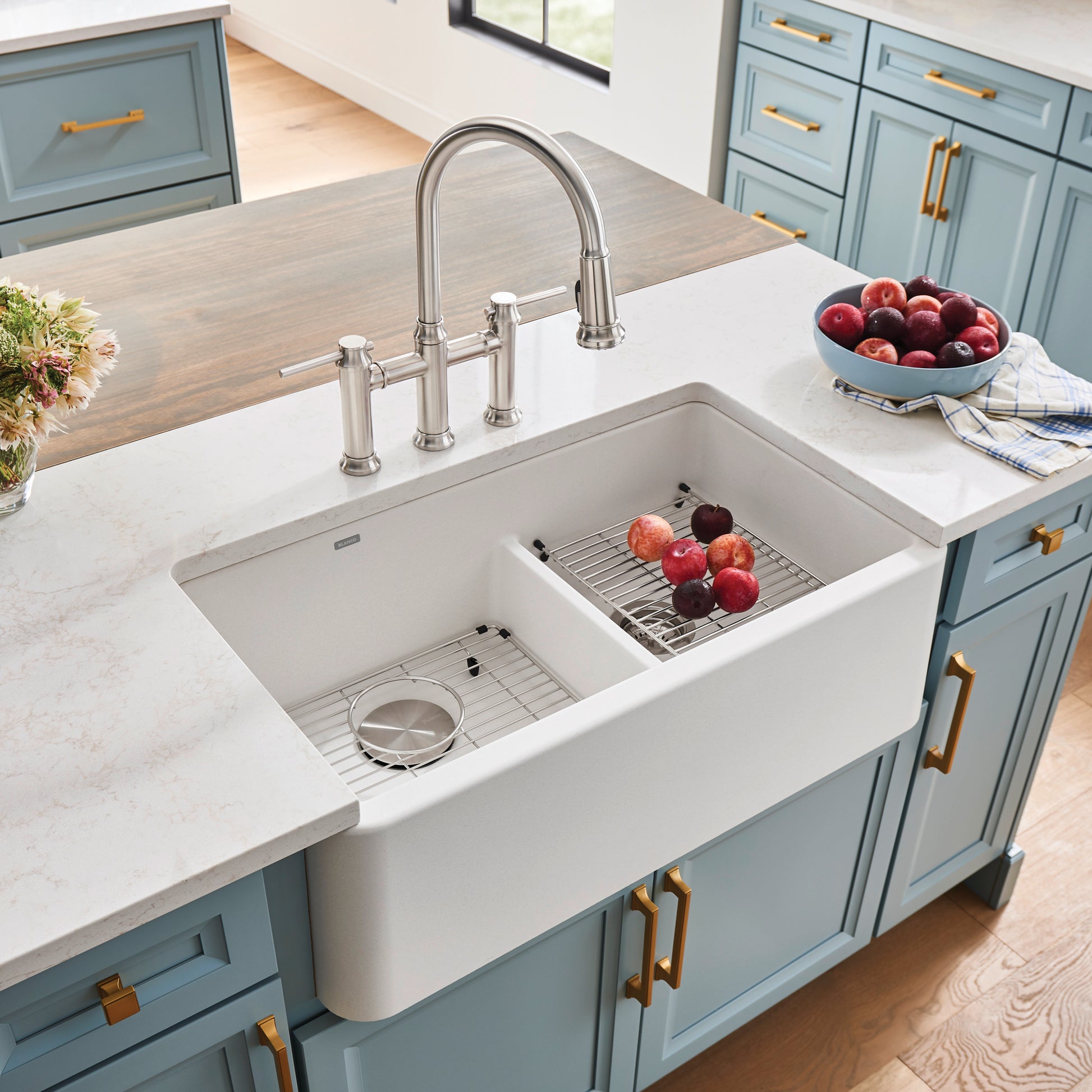 White double bowl farmhouse sink with low divide, stainless steel faucet, and grid inserts installed in marble countertop.