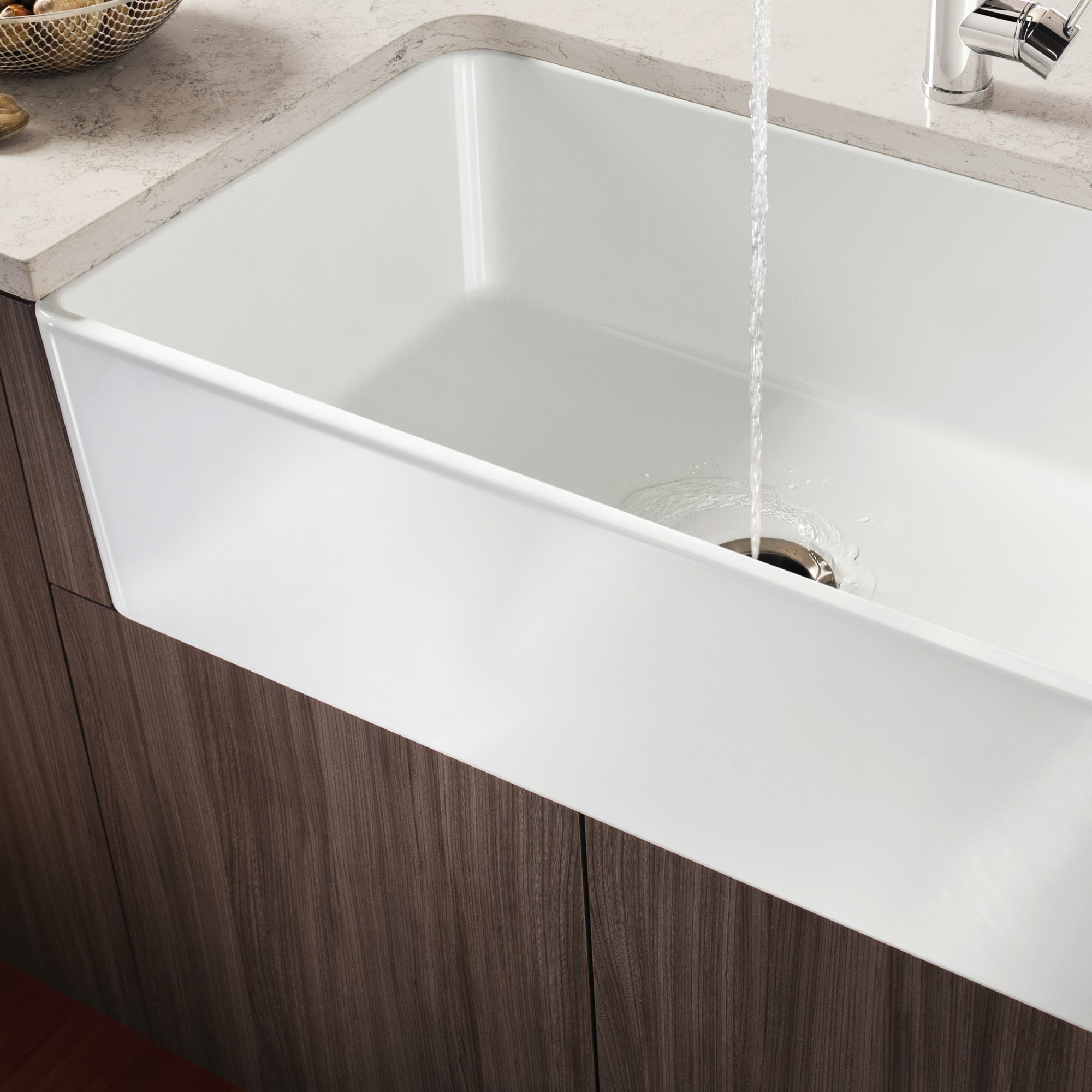 White porcelain single bowl farmhouse sink with curved apron front installed in dark wood cabinetry with water running.