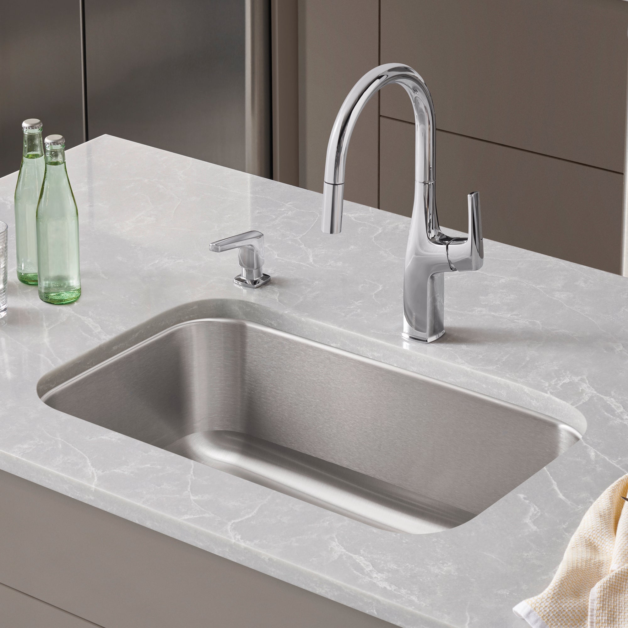 Stainless steel single-bowl undermount sink with chrome pull-down faucet and soap dispenser on marble countertop.