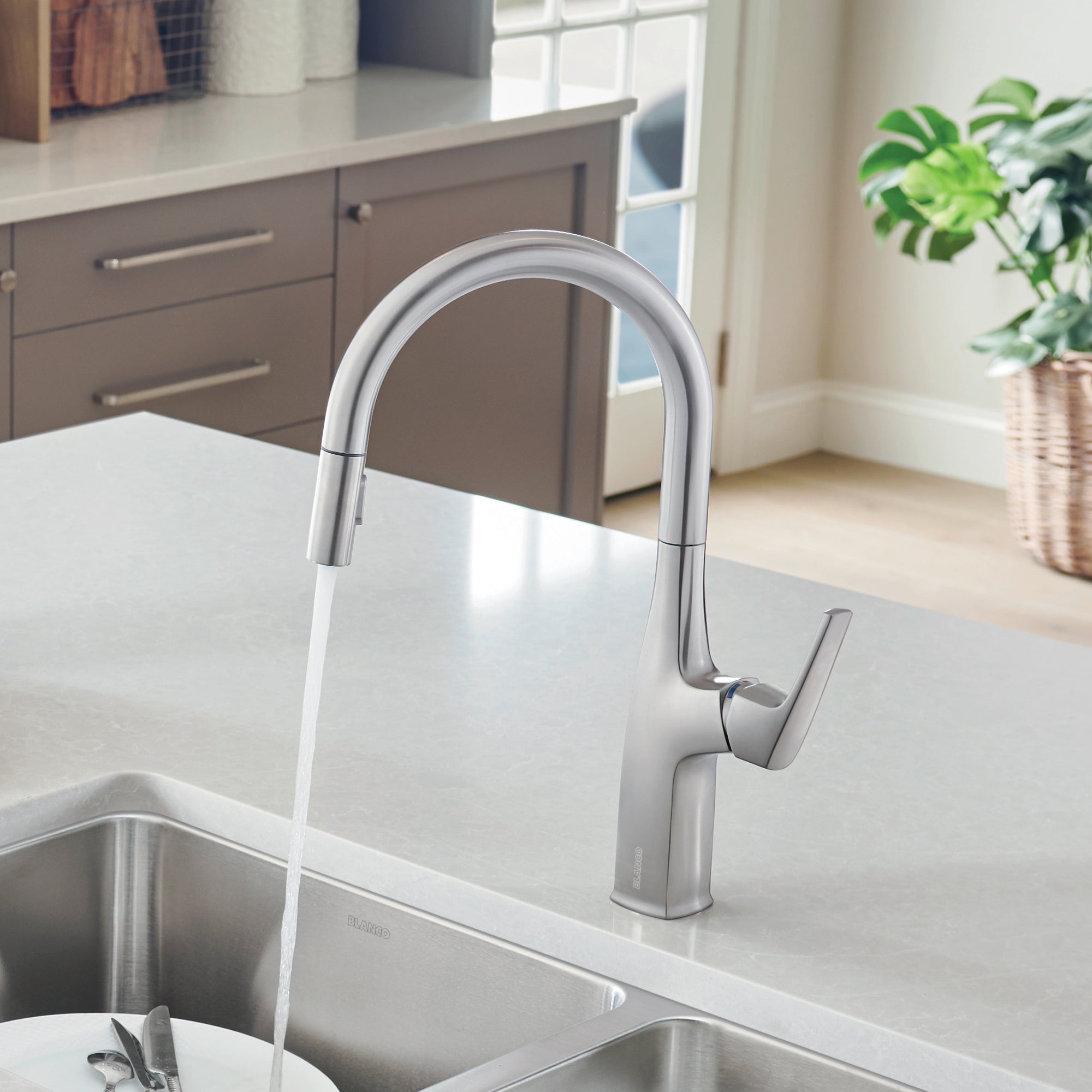 Stainless steel pull-down kitchen faucet with high arched spout and single lever handle over white countertop and sink.