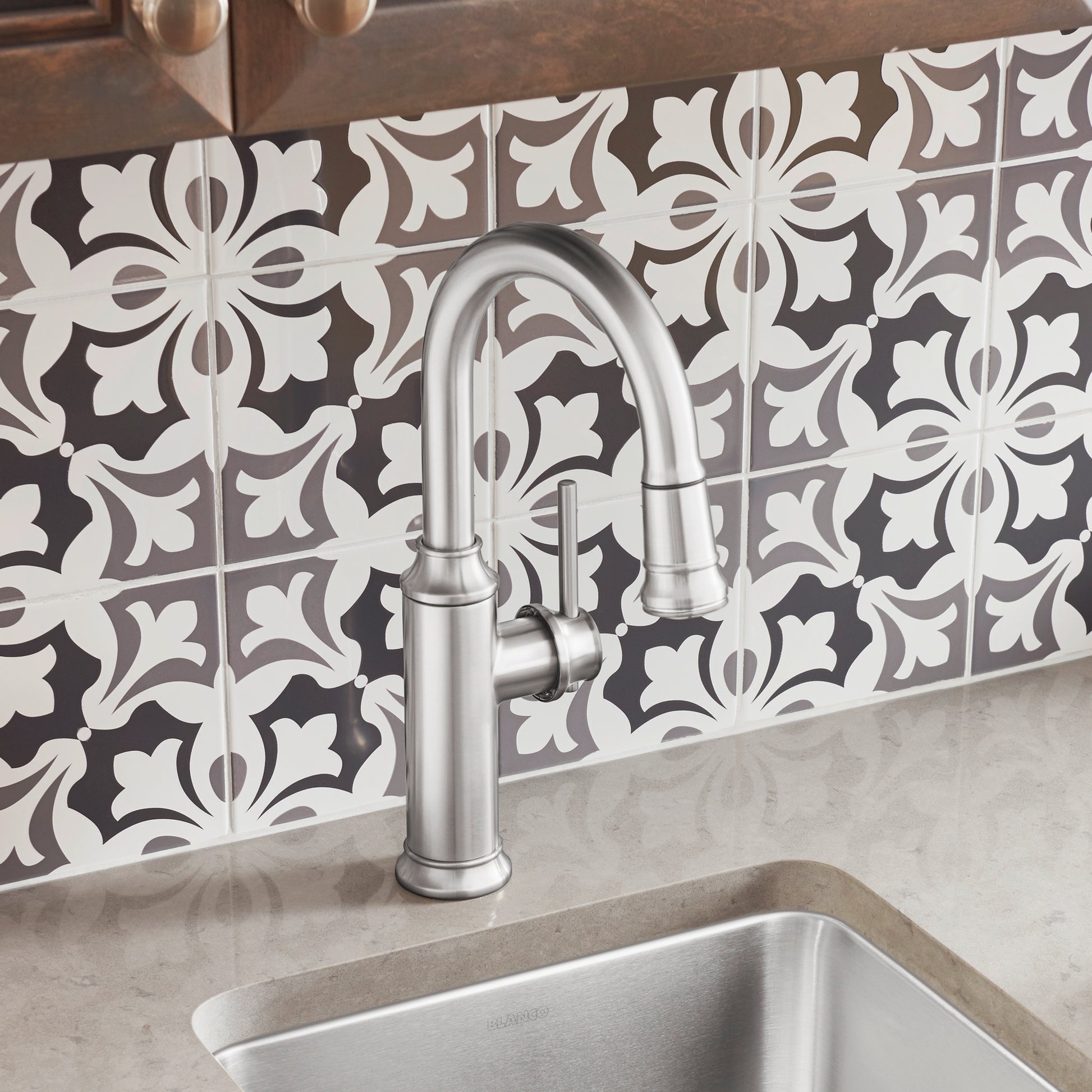 Stainless steel pull-down kitchen faucet with curved spout installed above undermount sink against decorative tile backsplash