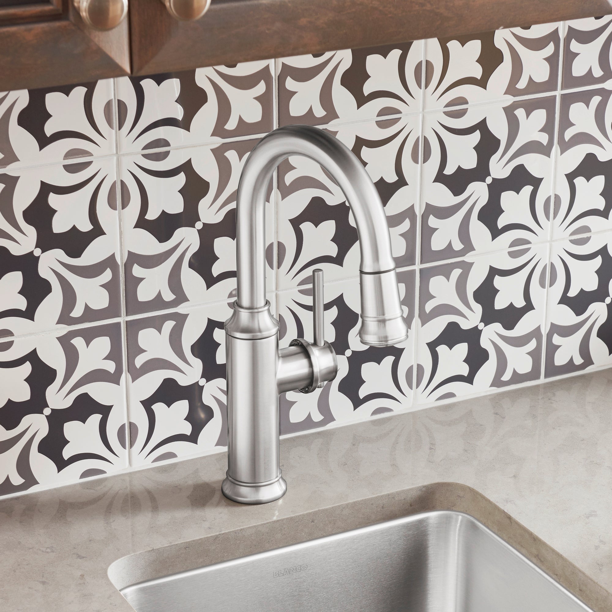 Stainless steel pull-down kitchen faucet with curved spout installed above undermount sink against decorative tile backsplash