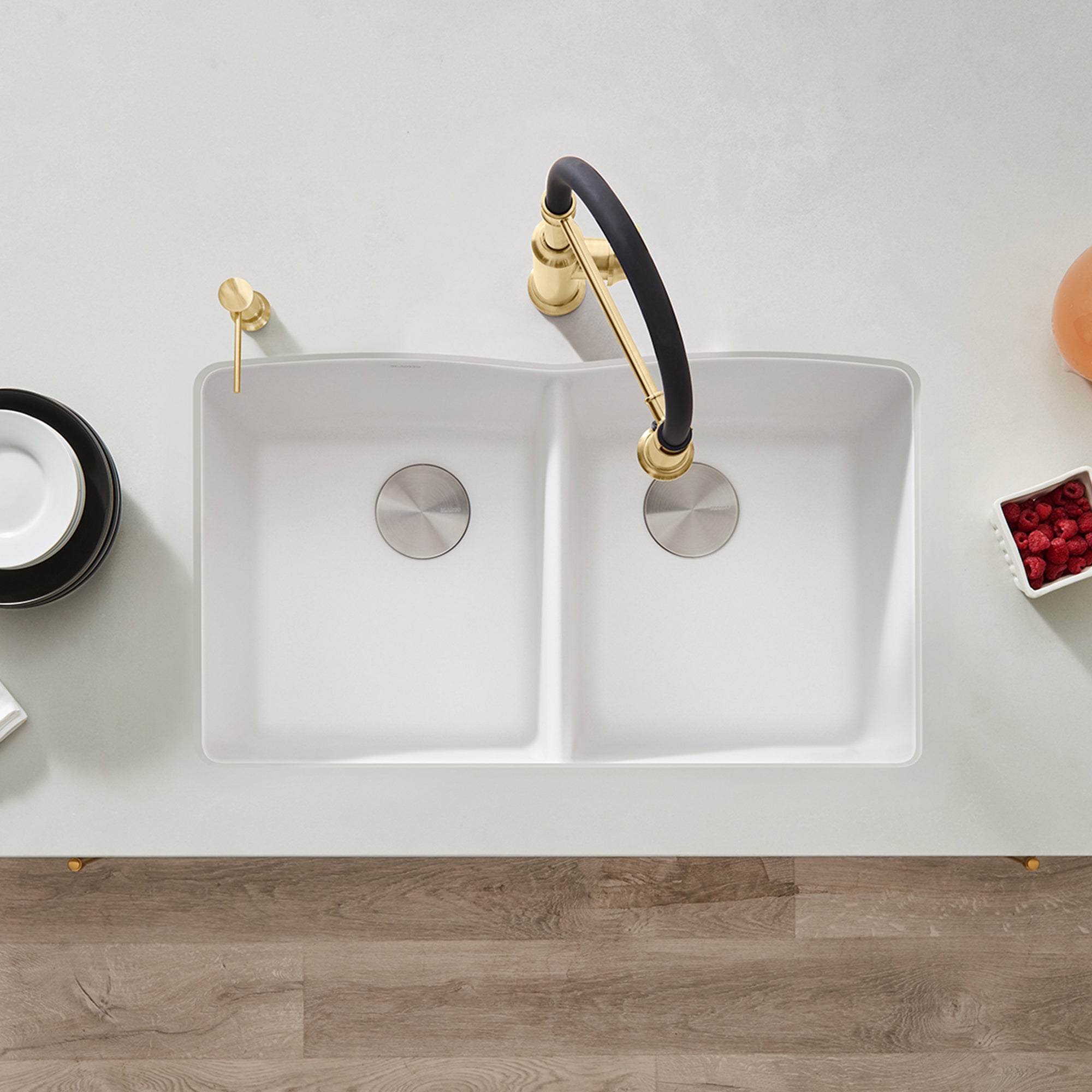 White equal double bowl undermount kitchen sink with dual drain strainers and black faucet with brass accents.