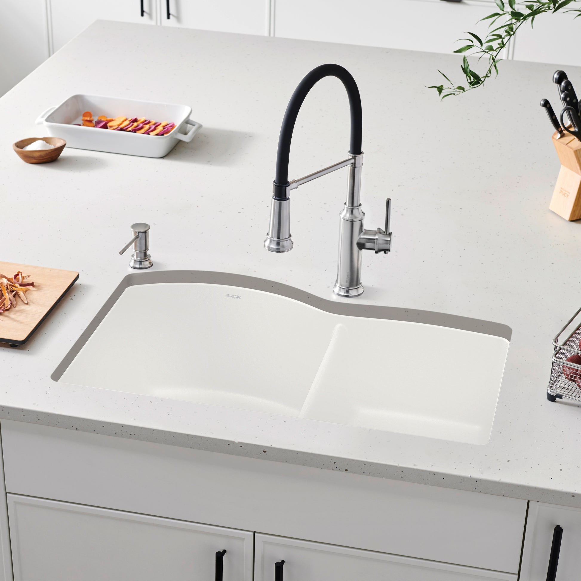 White undermount kitchen sink with single bowl and curved rim, installed in countertop with chrome faucet and soap dispenser.