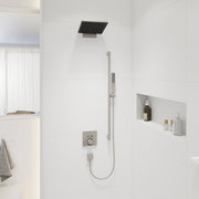 Brushed nickel rectangular shower head mounted on ceiling above white tile shower wall with handheld spray below.