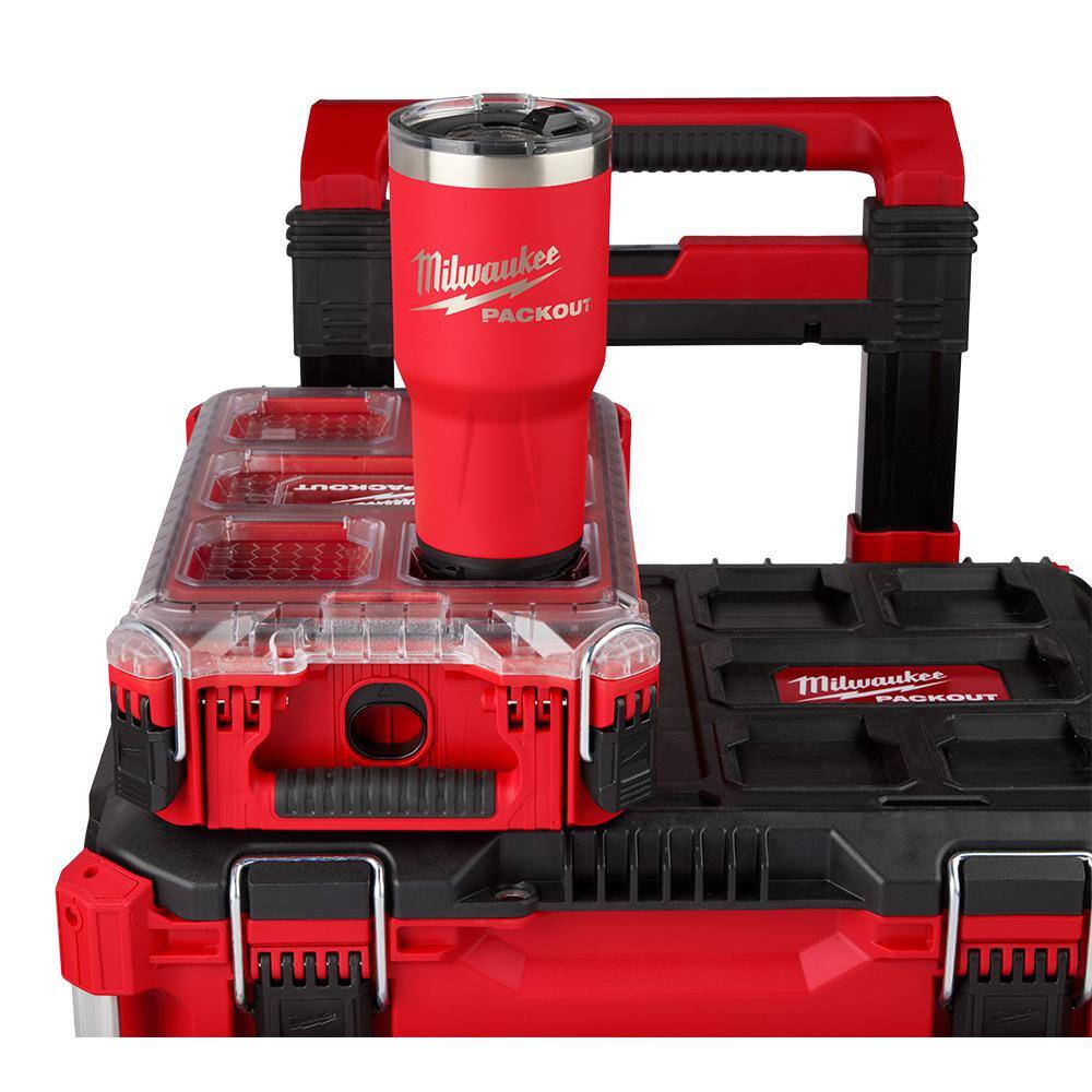 Red insulated tumbler with stainless steel top and black handle, mounted on red and black Packout modular storage system.