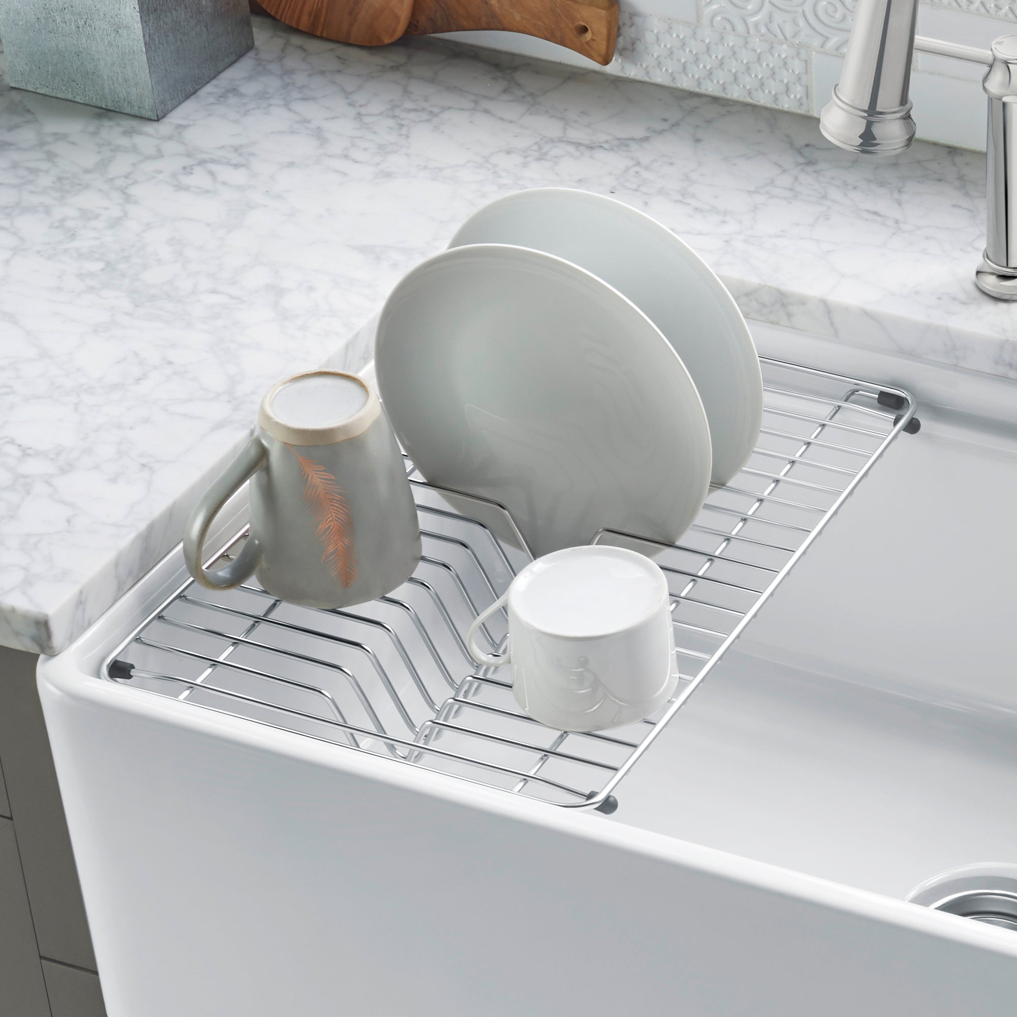 Stainless steel dish rack with white coating holding two plates and two mugs, installed in apron front sink.