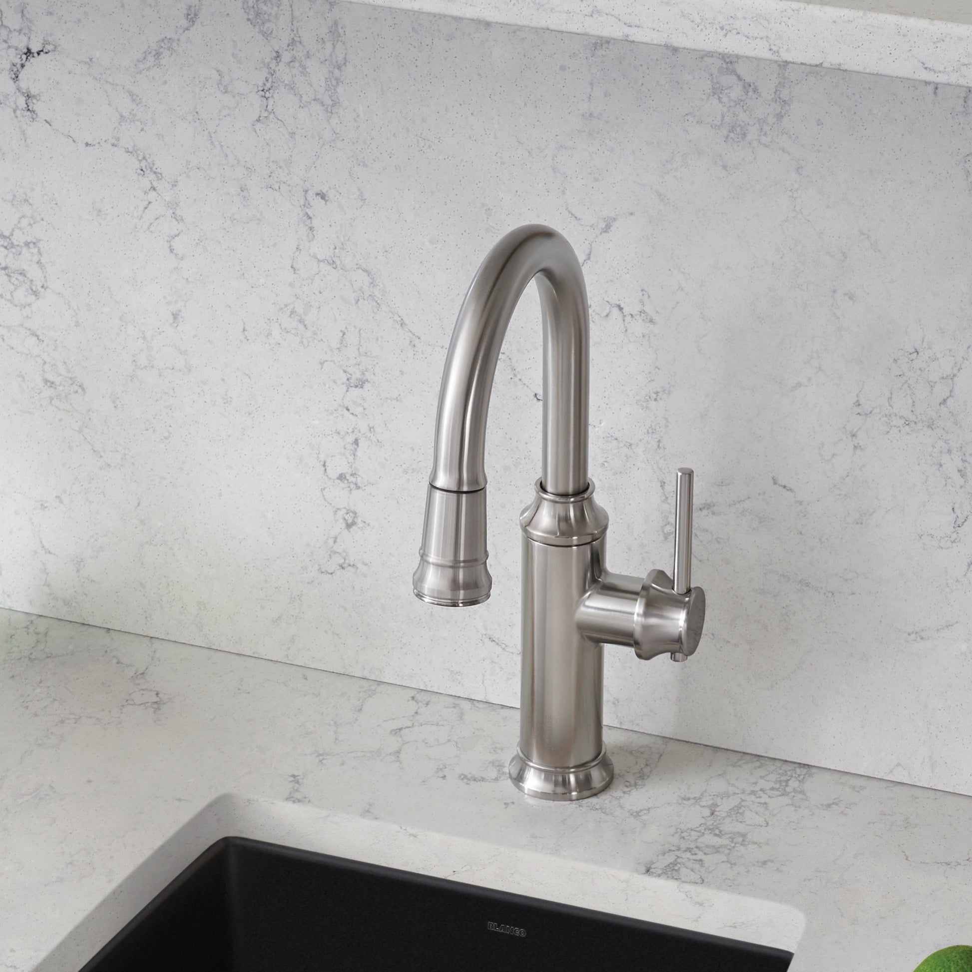Stainless steel pull-down kitchen faucet with curved spout and single lever handle mounted on marble countertop.