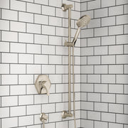 Polished nickel shower system mounted on subway tile wall with valve, handheld showerhead, and vertical bar.