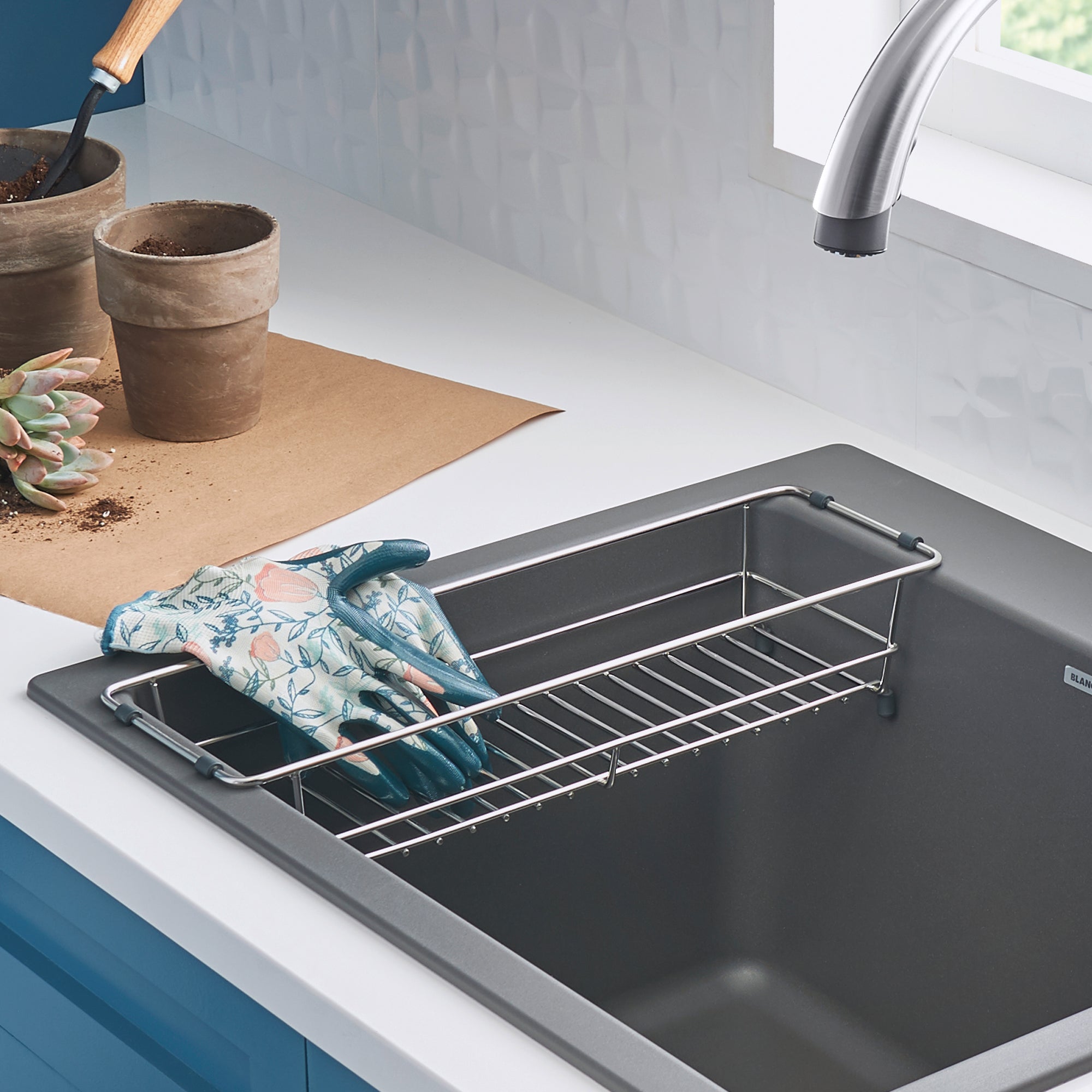 Stainless steel dish basket with handles sitting inside a dark laundry sink basin.