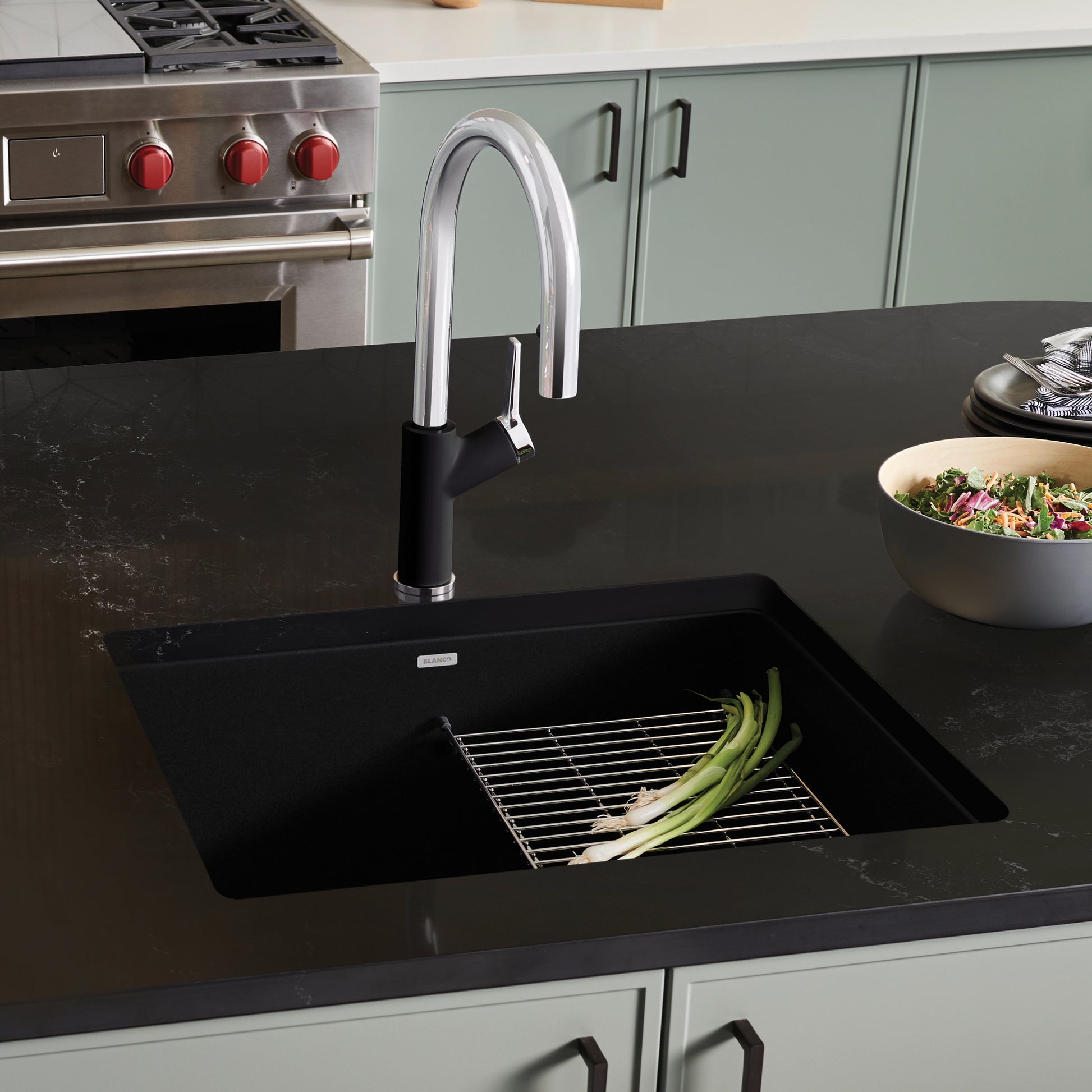 Coal black single bowl kitchen sink with chrome pull-down faucet installed in dark countertop.