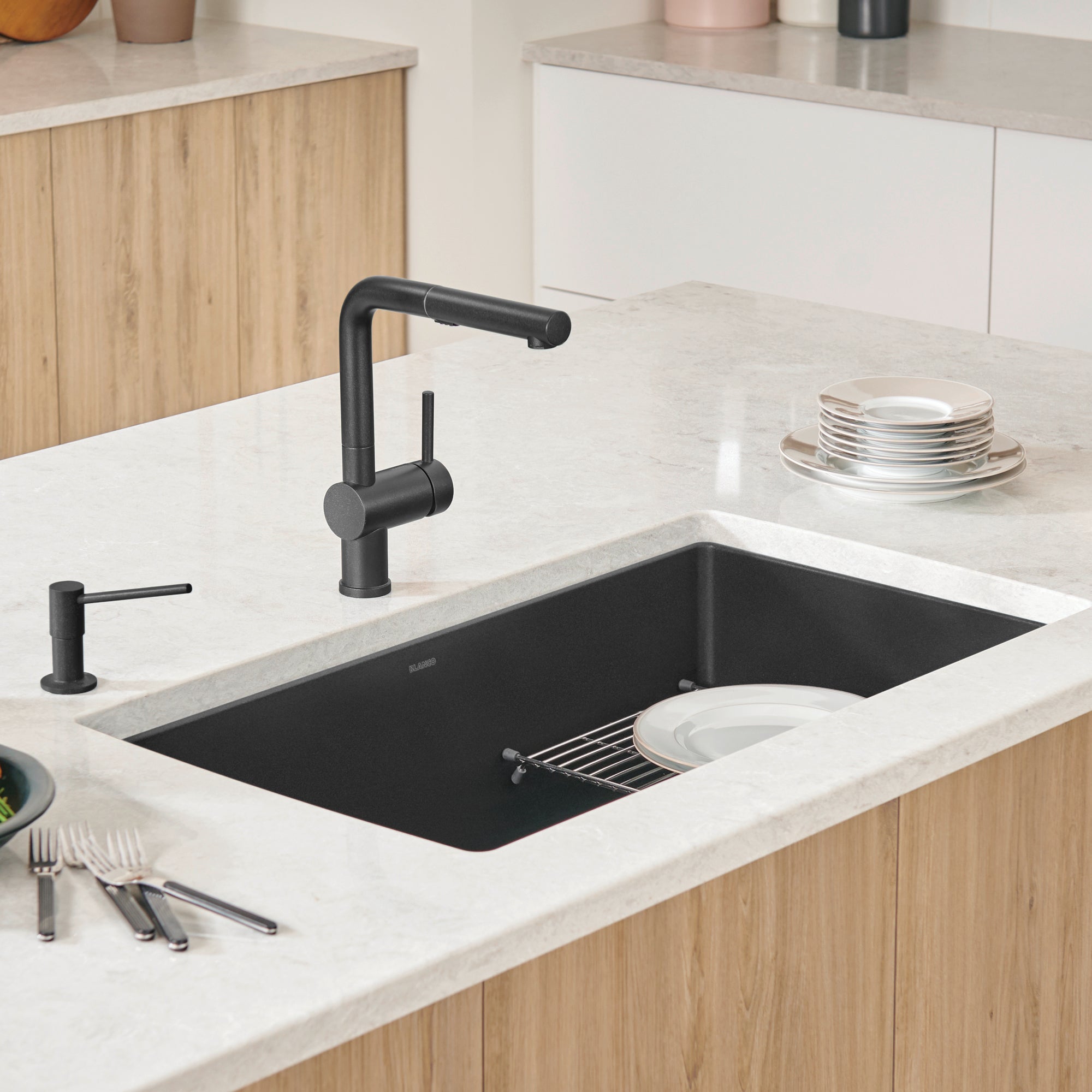 Anthracite undermount kitchen sink installed in white countertop with black faucet and wooden cabinetry.
