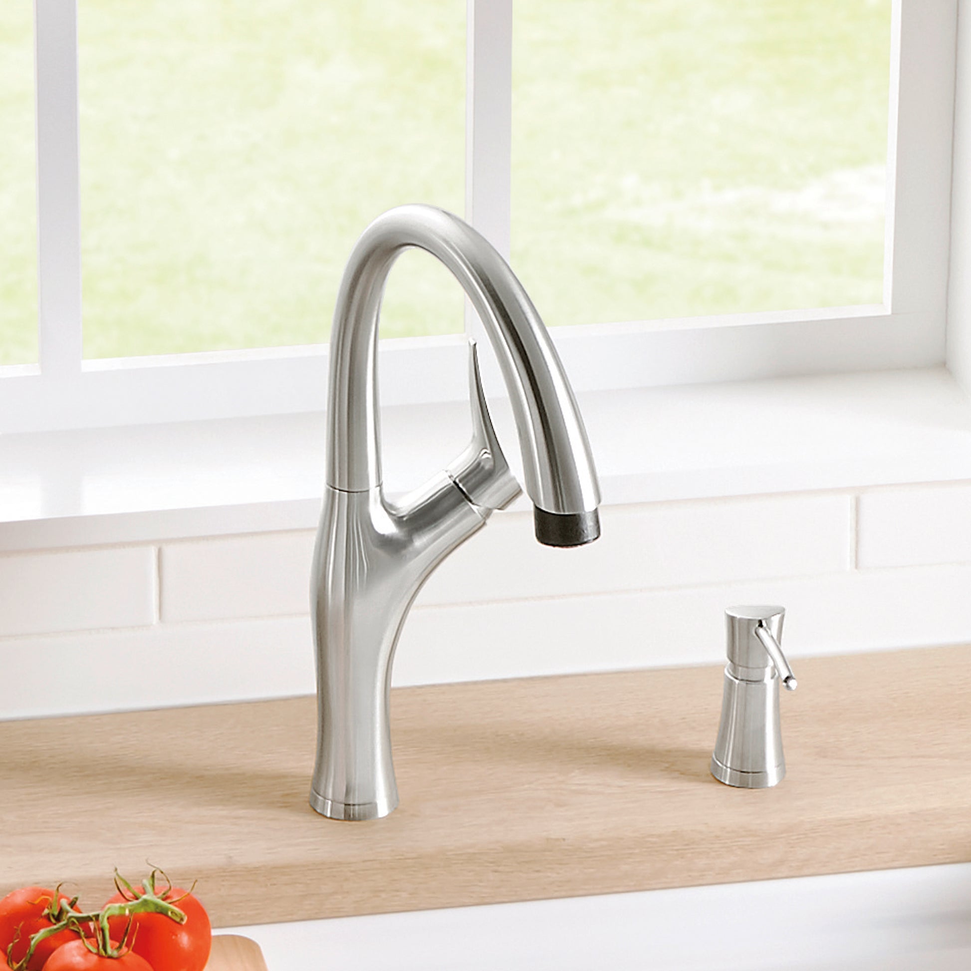 Stainless steel kitchen faucet with curved spout, pull-down spray head, and matching soap dispenser on wooden countertop.