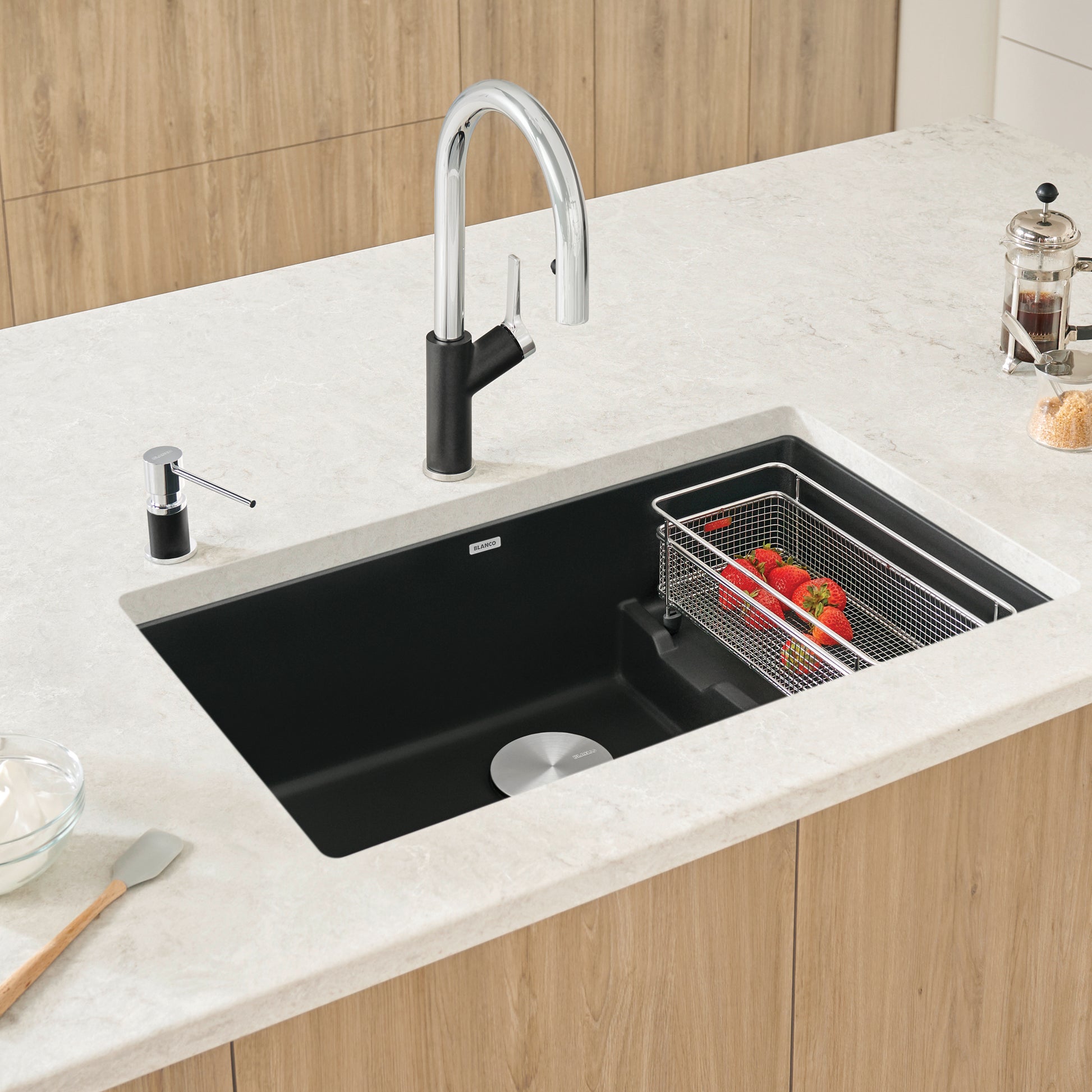 Coal black super single kitchen sink with chrome pull-down faucet and colander basket, installed in white countertop.