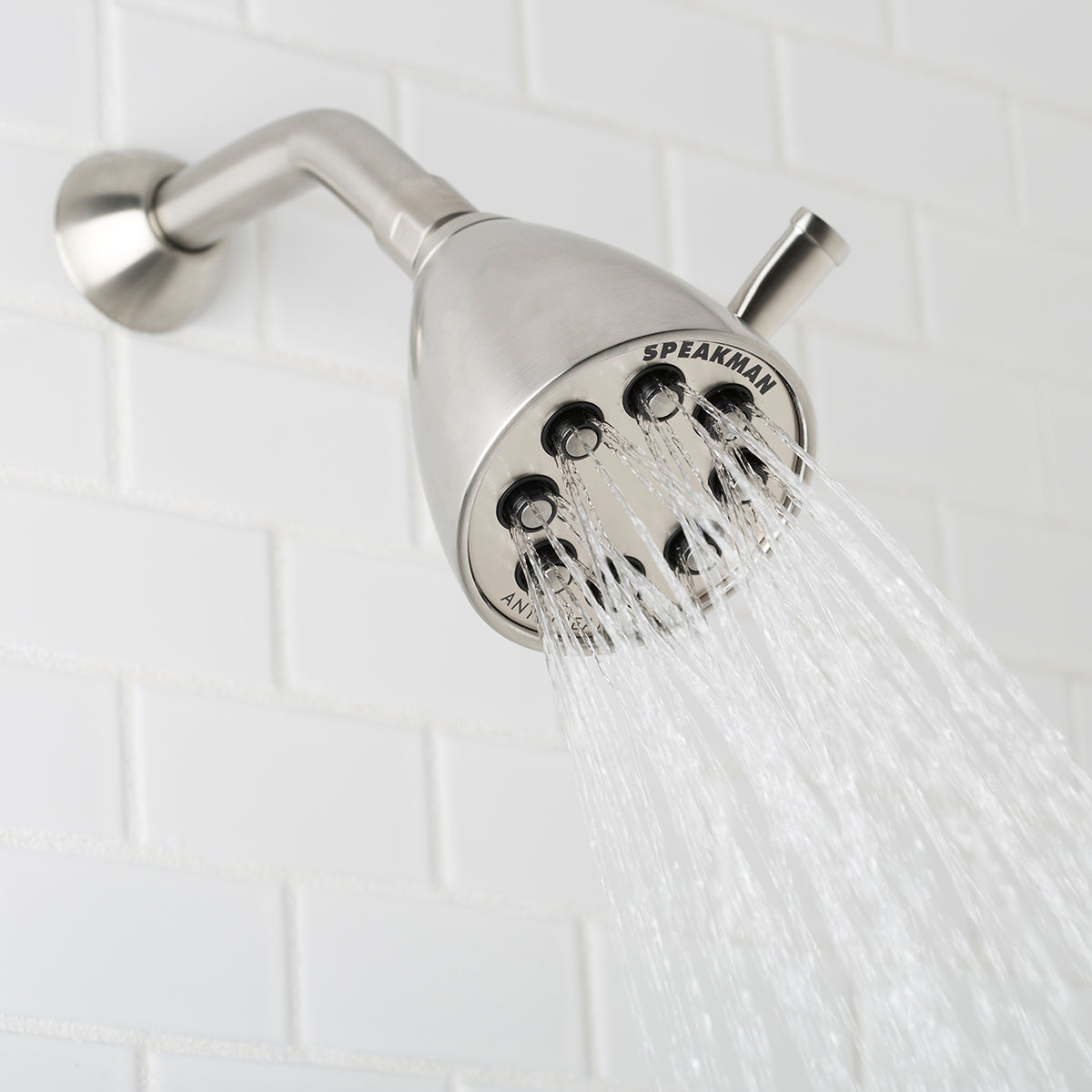 Brushed nickel shower head with multiple spray jets and curved arm mounted on white tile wall.