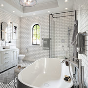 Polished nickel freestanding tub filler with curved spout and handheld showerhead mounted on white oval soaking tub.