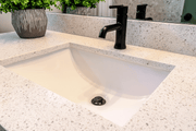 White rectangular undermount sink installed below speckled countertop with black rocker faucet.