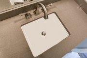 White rectangular undermount sink with flat bottom and single drain hole installed in beige countertop.