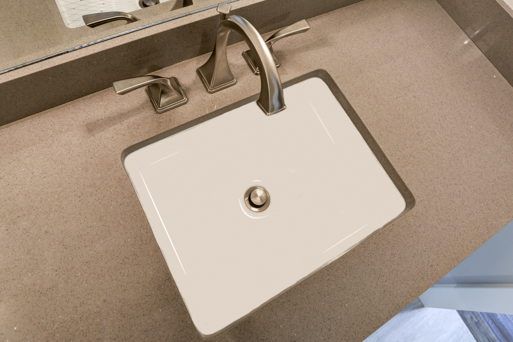 White rectangular undermount sink with flat bottom and single drain hole installed in beige countertop.