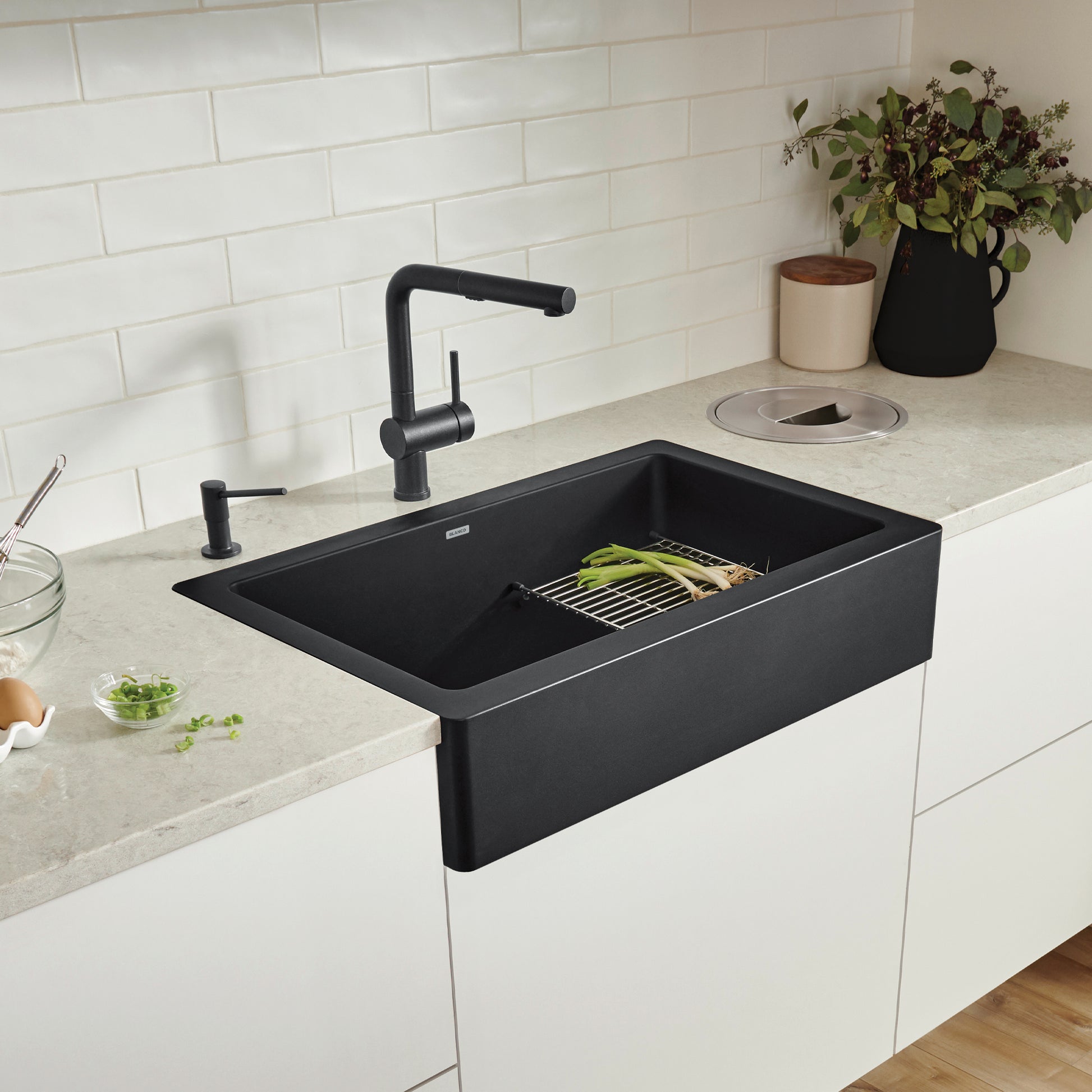 Coal black apron front farmhouse sink with single basin installed in white subway tile backsplash kitchen.