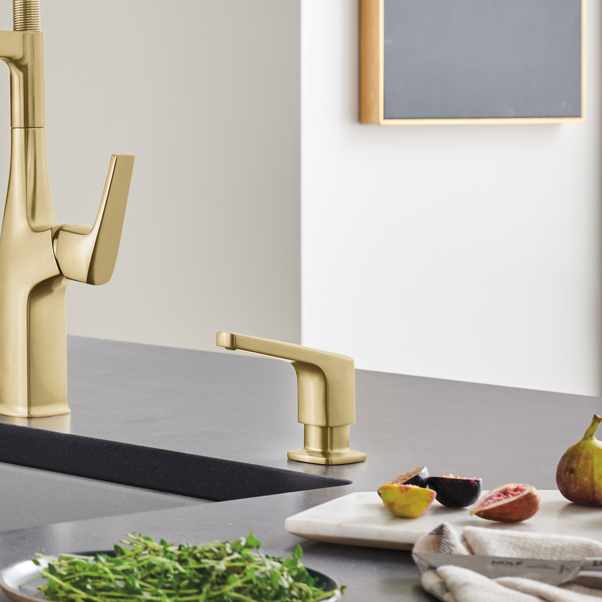 Satin gold soap dispenser with rectangular pump top displayed on a kitchen counter next to a faucet.