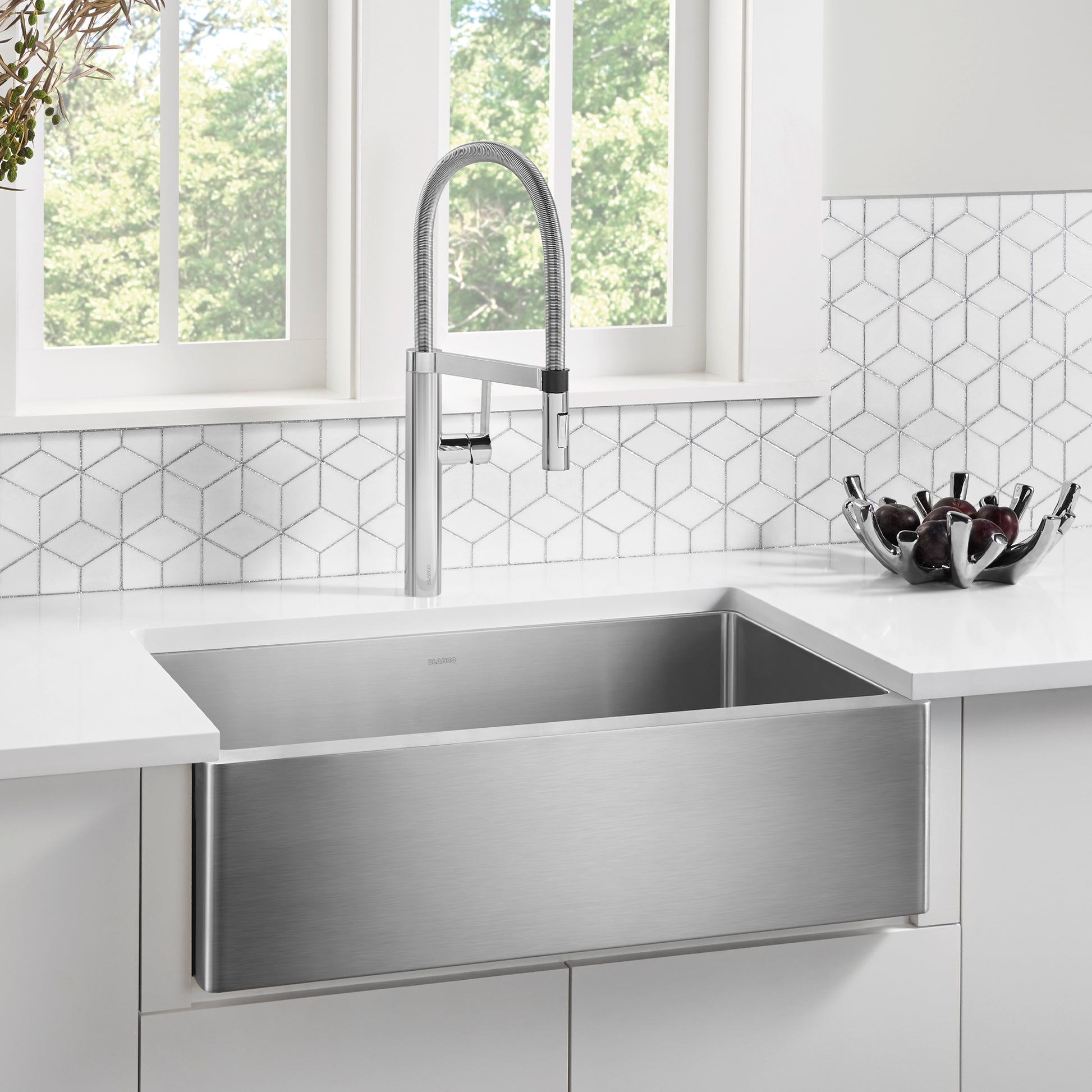 Stainless steel apron front sink with single basin and pull-down faucet in white kitchen.