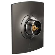 Matte black thermostatic valve trim with circular dial control and gold brass center post mounted on curved rectangular escut