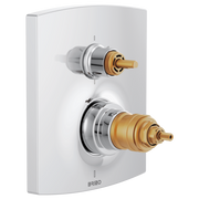 Chrome and brass thermostatic valve trim with two gold outlet ports mounted on white rectangular plate.