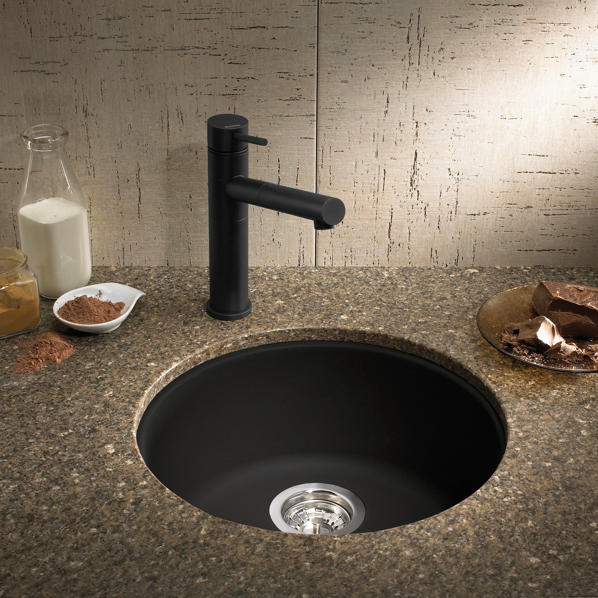 Round anthracite Silgranit bar sink with matching black faucet set in speckled countertop.