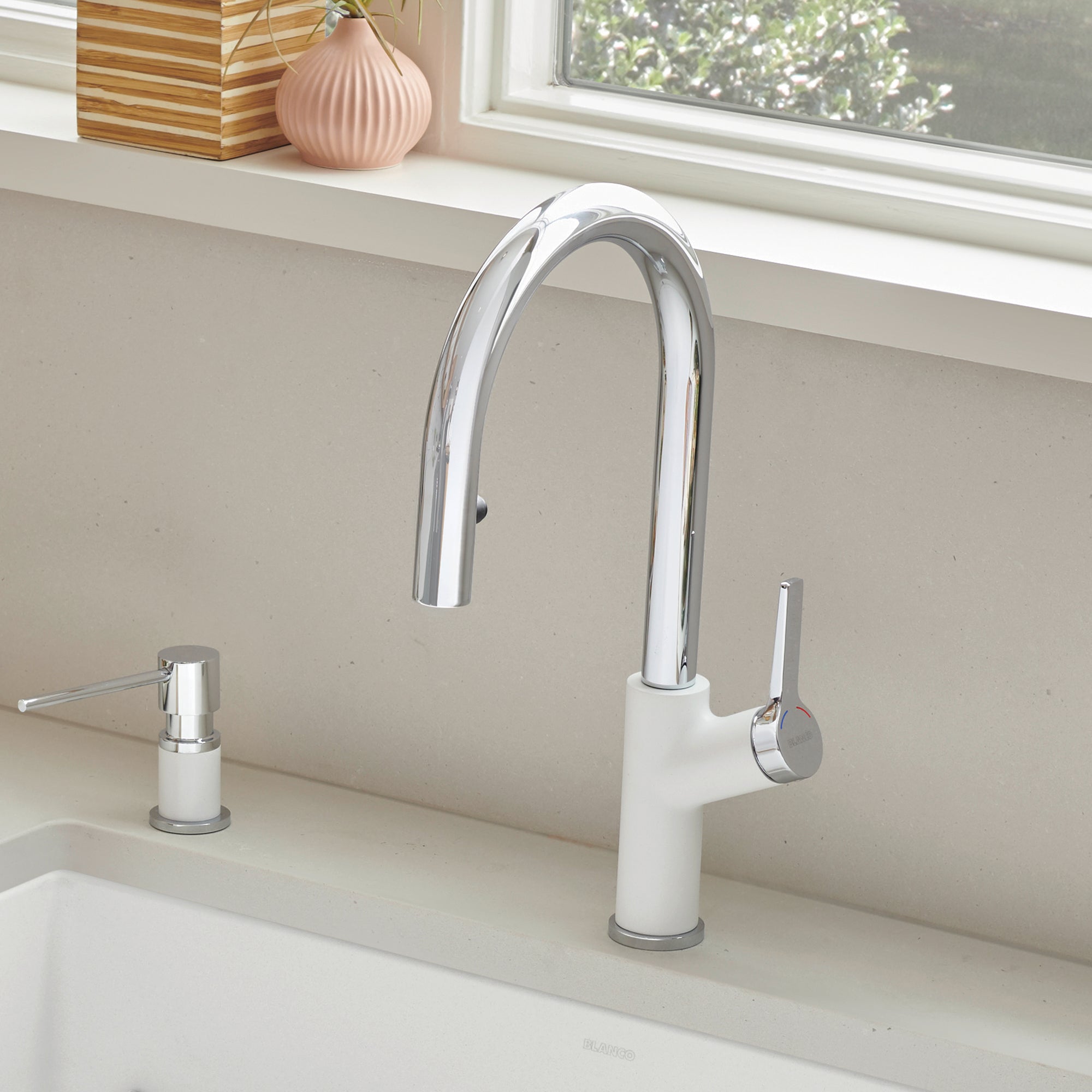 Chrome and white pull-down kitchen faucet with curved spout and single lever handle mounted on sink counter.