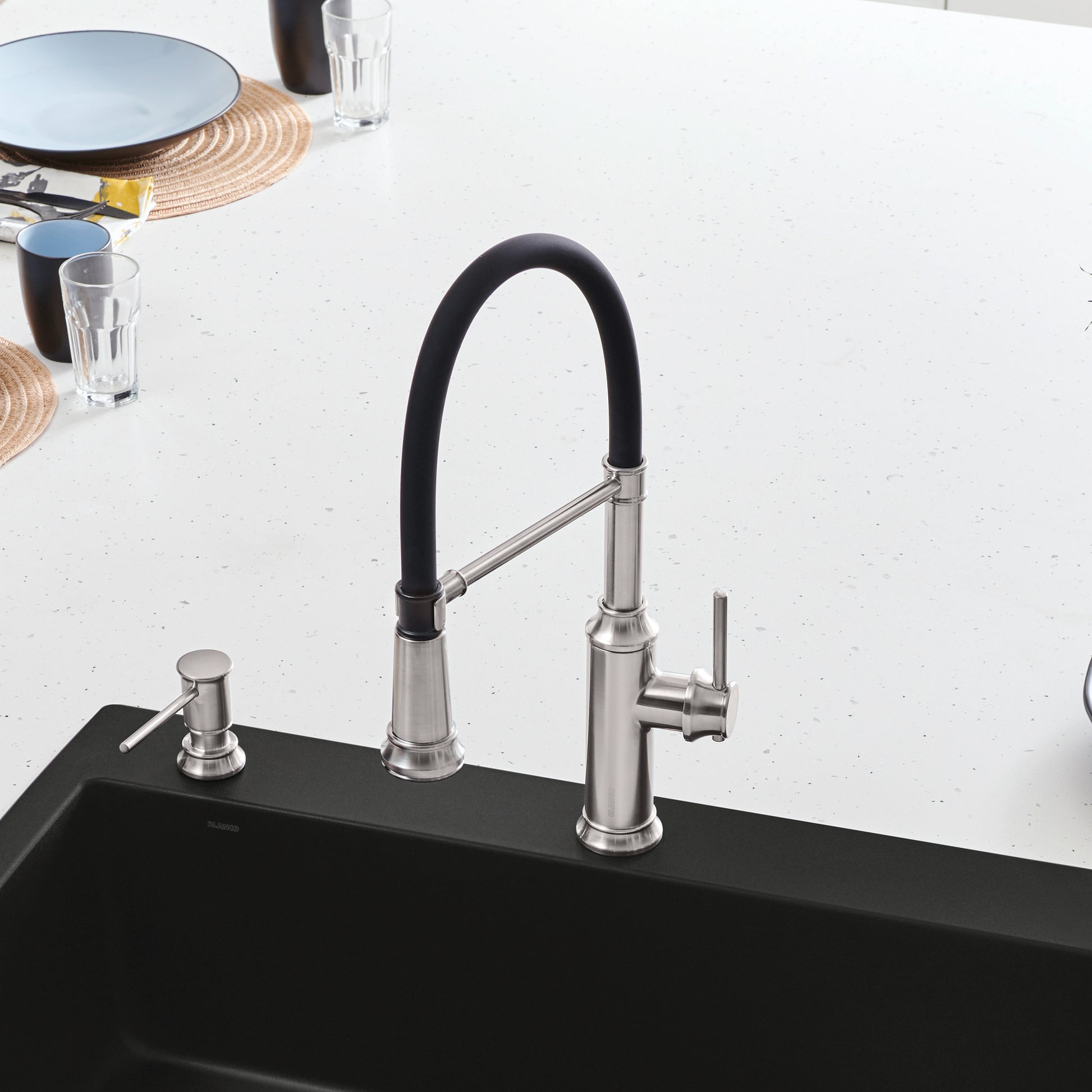 Stainless steel semi-pro kitchen faucet with black flexible hose and matching soap dispenser mounted on black sink.
